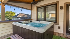 Un jacuzzi en una terraza de madera con vistas a una casa y árboles.