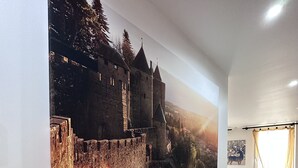 A living room with a large wall-mounted picture of a castle, a white sofa, and a small shelf with decorative items.