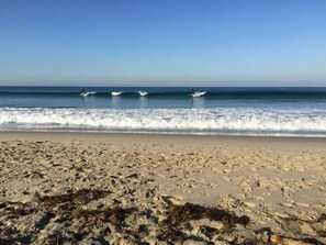 Une plage avec des vagues, un ciel dégagé et trois surfeurs dans l’eau.