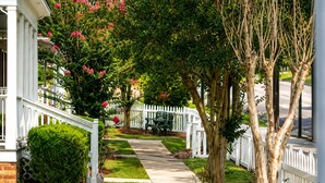 Une rue résidentielle bordée d’une clôture blanche en bois, avec un chemin et un banc.