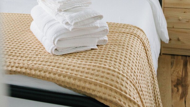 Un lit bien fait, avec des draps blancs, une couverture en tissu et une pile de serviettes pliées.