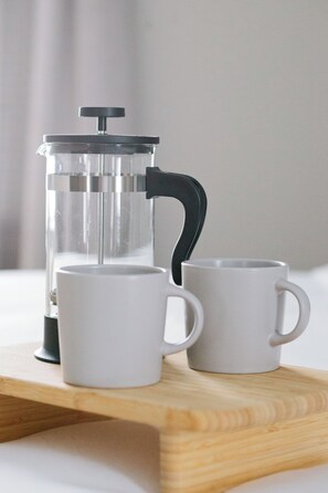 Eine French-Press-Kaffeemaschine auf einem Holztablett, daneben zwei weiße Tassen.