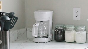 Une cuisine avec des armoires blanches, une machine à café et des bocaux remplis de nourriture sur le plan de travail.