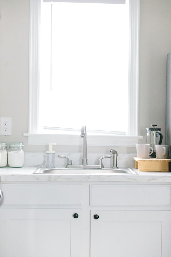 A kitchen with a sink, faucet, and window above it. There are jars and a coffee maker on the counter.