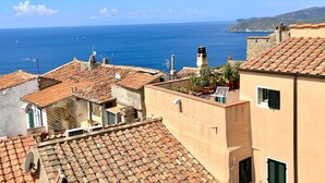 Un pueblo costero con tejados de tejas color terracota, un mar azul cristalino y una cadena montañosa en la distancia.