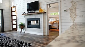 A modern living room with a fireplace, a flat-screen TV mounted above it, and a ceiling fan. - Moonlight Rest-Sleeps up to 4/Hot Tub (Broken Bow)