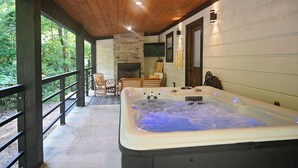 A hot tub with a stone fireplace, wooden deck, and a TV mounted on the wall. - Moonlight Rest-Sleeps up to 4/Hot Tub (Broken Bow)