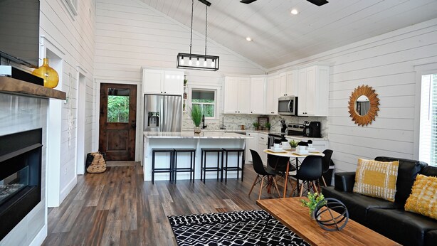 A spacious living area with a fireplace, a dining table with chairs, a black leather sofa, and a ceiling fan. - Moonlight Rest-Sleeps up to 4/Hot Tub (Broken Bow)