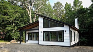 A modern two-story house with large windows and a sloped roof, surrounded by trees. - Moonlight Rest-Sleeps up to 4/Hot Tub (Broken Bow)