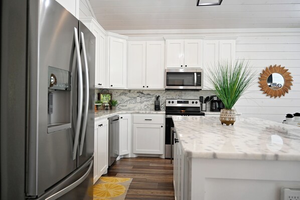 Kitchen features a refrigerator, microwave, and oven, along with a marble countertop and wooden floor.