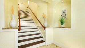 A staircase with wooden steps and a white handrail, leading to a landing with a wall-mounted light fixture and a framed quote. - Epic 6BR Beach View * Steps to Beach * Sleeps 20+ (Galveston)