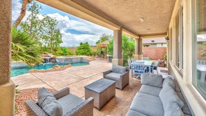 A covered patio with outdoor furniture, a swimming pool, and a view of the surrounding landscape.