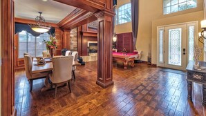 A spacious room with a wooden floor, a dining table with chairs, a pool table, and a fireplace.