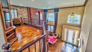A spacious room with a wooden floor, a billiards table, a fireplace, and a view of the outdoors through large windows.