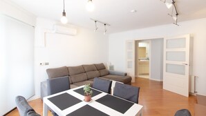 Een moderne woonkamer met een bank, een eettafel met een potplant en een keuken op de achtergrond.