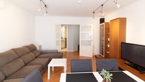 Een moderne woonkamer met een bank, een eettafel, stoelen, een televisie en een boekenkast.