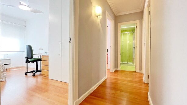 Een hal met houten vloer, een bureau met stoel, een plafondventilator en een douchedeur met groene tint.