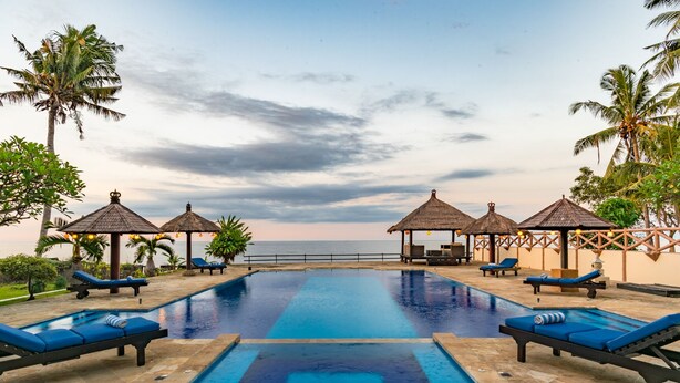 A pool area with lounge chairs and thatched-roof gazebos, overlooking the sea. - Villa Bukti Paradise (Kubutambahan)