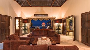 A spacious living room with a large brown sofa set, a coffee table, and a view of the sea through a large window. - Villa Bukti Paradise (Kubutambahan)