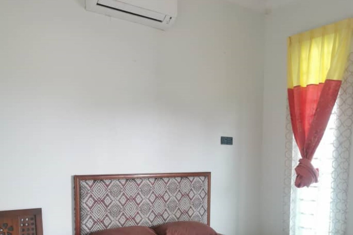 A bedroom with a bed, a wooden nightstand, a patterned headboard, and an air conditioning unit.