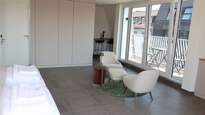 A modern room with a bed, two chairs, a small table, and a view of the outside balcony. - Studio mit Küche 12 (München)