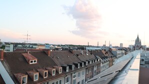 A cityscape with multiple buildings, including a prominent church with a spire, and a variety of rooftops with different architectural styles. - Studio mit Küche 12 (München)