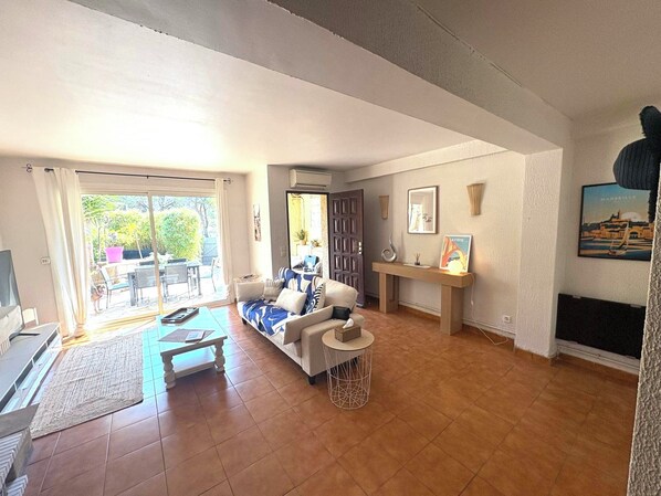 A living room with a sofa, coffee table, and a TV. There is a sliding glass door leading to an outdoor area.