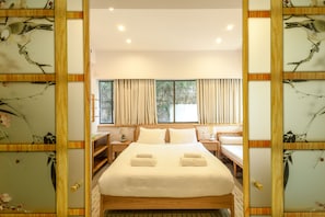 A spacious bedroom with a large bed, two bedside tables, and a view of greenery through the windows. - Charming 2BR Apt w a Breathtaking Patio (Tel Aviv)