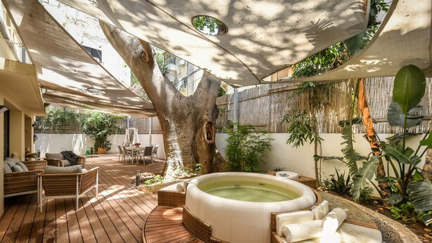 A wooden deck with a hot tub, wicker furniture, and tropical plants. - Charming 2BR Apt w a Breathtaking Patio (Tel Aviv)