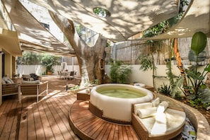 Una terraza de madera con un jacuzzi, muebles de mimbre y plantas tropicales.