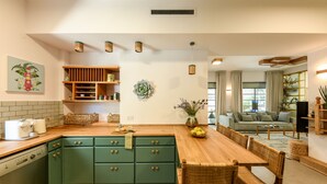 A modern kitchen with green cabinets, a wooden dining table, wicker chairs, and a central island with a vase of flowers. - Charming 2BR Apt w a Breathtaking Patio (Tel Aviv)