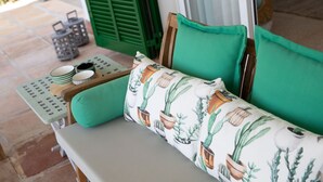 A bench with a cushion featuring a cactus pattern, a small table with a tray of dishes, and a green door in the background. - Chalet Can Contestí (Llucmajor)