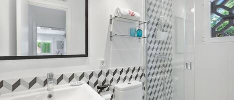 A modern bathroom with a white sink, a toilet, a glass shower enclosure, and a mirror.