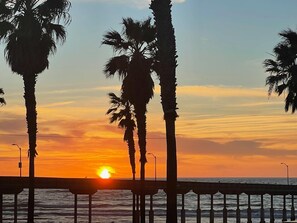 Ein Sonnenuntergang über dem Meer mit Palmen und einem Steg.