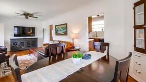 Uma sala de estar moderna com uma mesa de jantar, cadeiras de madeira escura, um sofá, uma televisão e um ventilador de teto.