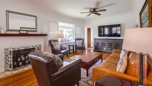 Uma sala de estar com sofá, poltronas, mesa de centro, televisão e ventoinha no teto.