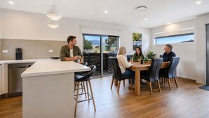 Een moderne keuken met een centraal eiland, een eethoek met stoelen en een uitzicht door de glazen deur.