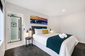 A hotel room with a bed, a nightstand, a painting, and a glass shower enclosure.