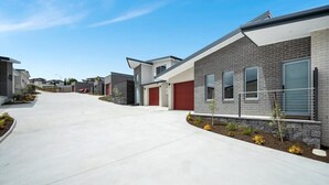 Een moderne woonstraat met huizen met bakstenen gevels, rode garage deuren en kleine voortuinen met planten.