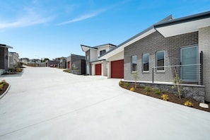 Een moderne woonstraat met huizen met bakstenen gevels, rode garage deuren en kleine voortuinen met planten.