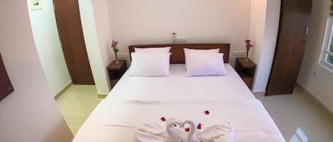 Une chambre d’hôtel avec un grand lit, deux tables de chevet, une petite table, une armoire en bois et une fenêtre.