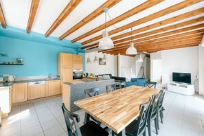 Een moderne keuken met houten kasten, een eethoek met een houten tafel en een televisie in de woonkamer.