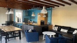 Ein modernes Wohnzimmer mit einem Holzesstisch, blauen Sofas und einer Küchenzeile mit Holzschränken und einer blauen Akzentwand.