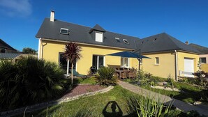 Ein zweistöckiges Haus mit gelber Fassade, schwarzem Dach und einer kleinen Veranda.