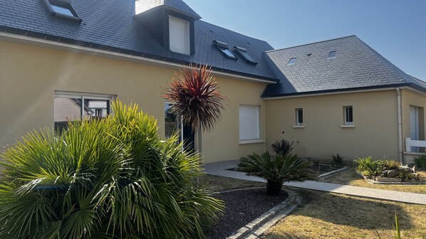 Une maison moderne avec un toit en pente, une porte d’entrée et un petit jardin agrémenté de différentes plantes.