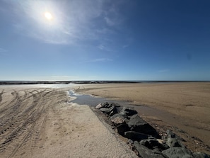 A sandy beach with tire tracks and a rocky area.