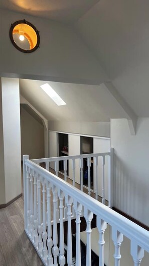 Una escalera con balaustres blancos, barandilla blanca y una lámpara en el techo.