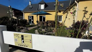 Ein gelbes Haus mit Terrasse, Gartenmöbeln und einem Schild.