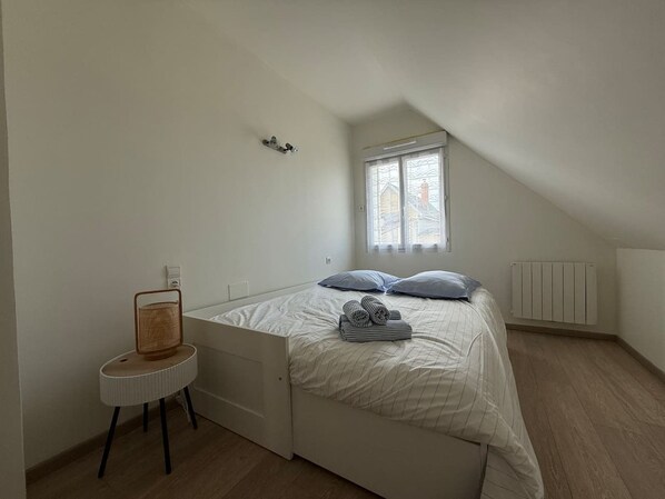 Un dormitorio con una cama, una mesita, un radiador y una ventana.
