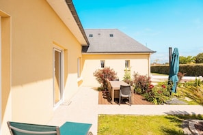 A yellow building with a patio area, a table with chairs, and a green umbrella. - Villa Jersey (Saint-Germain-sur-Ay)